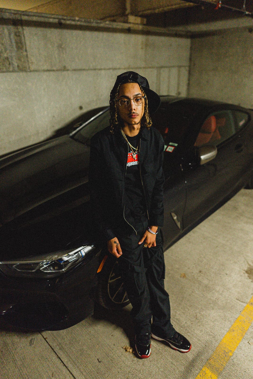Jayggm standing in front of a black coupe in a parking garage